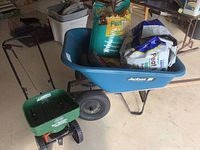 Jackson blue plastic wheelbarrow with lawn bags inside and Scotts Turf Builder EdgeGuard Mini spreader in front