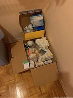 Box containing various lightbulbs, mostly in packaging including CFL and LED bulbs of different sizes and shapes.