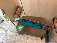 Photo showing a teal umbrella with a blue curved handle lying on an ottoman with a navy umbrella and cane nearby.
