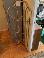 Tall gold-tone metal corner stand with three curved wire shelves, placed in corner against wall and adjacent door frame