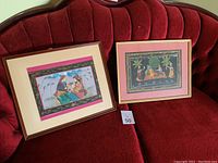 Both framed Indian fabric art paintings on red velvet couch, showcasing full view of lot
