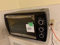 Side angle of black Oster microwave oven showing front door with glass window and 3 control dials on the right side.