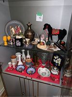 Shelf display of various decorative ceramics, glassware, and figurines including a black horse, floral plates, and glass goblets.