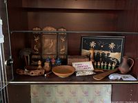 Photo showing the full collection displayed in a cabinet, featuring the folding wooden panel with bird inlays, painted bottles, wooden tray items and other small decorative pieces.