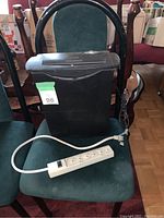 Black paper shredder next to white extension cord placed on a green fabric chair