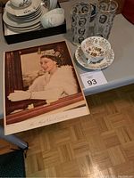 Photo showing late Queen Elizabeth II large print, four glasses with British Prime Ministers, and a tea cup with saucer