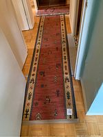 First image shows one of two runner rugs laid out in a hallway; reddish with black and beige tribal designs with beige border.
