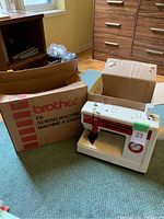 Brother 810 sewing machine on carpet floor next to original large Brother branded cardboard box and another smaller plain cardboard box.