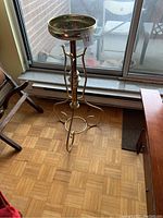 Full view of the metal stand placed on wooden floor near a window, showing its overall height and tripod leg design.