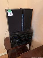 Stereo system components stacked with two black speakers on top of a dark wood side table in corner of room.
