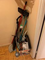 Photo showing the assortment of cleaning supplies including the vacuum box, mops, broom, dustpan, and brushes.