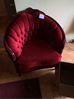 Front angle view of chaise lounge showing tufted red velour upholstery and carved wooden frame.