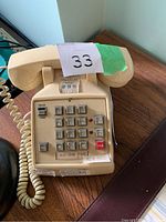 Full view of vintage beige push-button landline telephone showing keypad, handset, and coiled cord on wooden surface.