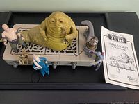 Wide shot of playset on black base with integrated Jabba sculpt, four additional figures and instruction manual.