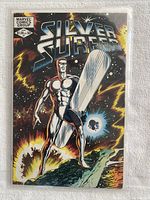 Front cover of the Silver Surfer Vol. 2 #1 comic book featuring Silver Surfer in a cosmic setting with bright colors and details, held in clear protective sleeve on a white towel.