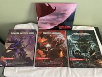 Three Dungeons & Dragons books placed side by side with a folded playing board behind them, showing detailed cover art with fantasy creatures.