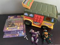 Photo showing the 1989 TMNT Party Wagon toy, two loose figures (Super Shredder and Sewer Michelangelo), and packaged Donatello figure.
