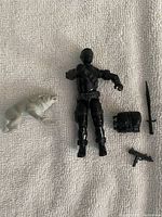 Snake Eyes figure lying with accessories spread around: wolf, backpack, sword, and submachine gun visible.