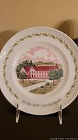 Front view of tenth Avon anniversary plate with building illustration and gold floral border.