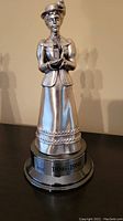 Silver-tone Avon commemorative lady figurine on round base with inscription '1886-1986'.