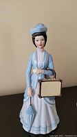 Full view of the porcelain figurine featuring Mrs. Albee in blue attire holding a parasol and straw bag.