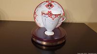 Porcelain teacup and matching saucer with red and gold details, mounted on wooden display base with engraved honor society award plaque for 1997
