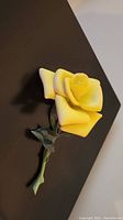 Yellow rose porcelain figurine showing detailed petals and green stem with leaves.