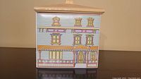 Front and side view of house-shaped ceramic canister with decorative painted windows, door, and shingles.