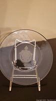 Front view of the clear glass plate with embossed door knocker-like design in center on display stand.