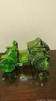 Side view of green glass figurine modeled after Haynes-Apperson 1902 car on dark polished surface.