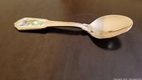 Silver-tone teaspoon with decorative floral handle photographed on a brown surface.
