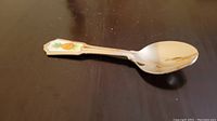 Full view of the teaspoon resting on dark surface showing the pineapple design on handle and polished spoon bowl.