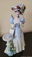 Front view of the detailed porcelain figurine with the woman in vintage attire and three bluejays.