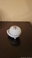 Front angle view of the porcelain egg-shaped box showing floral decoration and handle detail.