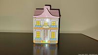 Front view of small decorative canister shaped like a miniature town house with colorful design detail.