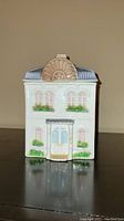 Porcelain canister shaped like a two-story house with windows, door, and roof details