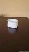 Small white porcelain basket with woven pattern on a dark reflective surface