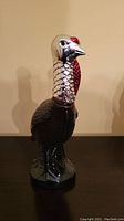 Front view of ceramic wild turkey decanter bottle with painted red, black, and silver details, displayed on black surface against plain wall.