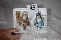 Hand holding a foam container with two Santa Claus ornaments in original packaging, wrapped in plastic, showing limited edition certification tags