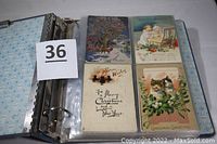 Photo of binder with plastic sleeves containing multiple Christmas postcards depicting kittens, children, Santa Claus, and floral holiday designs.