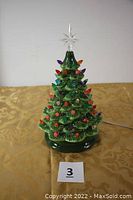 Full frontal view of the green ceramic Christmas tree with multicolored bulbs and clear star top, showing plugged-in electrical cord at the rear base.