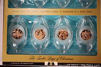 Photo showing the six bronze medallion ornaments in clear Lucite holders arranged in the original packaging, each depicting different motifs from the 12 Days of Christmas carol.