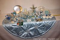 Full view of blue Christmas tree skirt with assorted ornaments arranged on top, showing variety of sizes and colors.