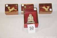 Four ceramic/porcelain ornaments in original red boxes including three reindeer and one bell.