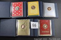 Five cloth-covered presentation folders arranged open, each showing the first greeting card and associated bronze medallion for the years 1983 through 1987.