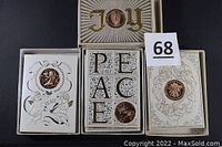 Four holiday greeting cards with central bronze medallions, designs include 'JOY' and 'PEACE' themes with angelic and ornamental illustrations.
