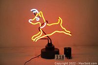 Neon light of a leaping reindeer lit up in orange and white on a black base with a cord attached, photographed against a neutral background.