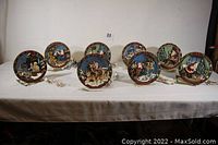 Eight illuminated Christmas-themed decorative plates arranged in a line, all plugged in, showing their detailed 3D holiday scenes and integrated lighting effects.