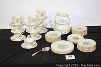 Full set of china including stacked cups and plates, teapot, and cheese cutter shown on black cloth background.