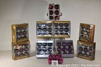 Seven boxed sets of Christmas balls by Martha Stewart and one set by Sandra Lee, arranged in a grid. Mostly purple-colored glass ornaments with both shiny and matte finishes. One set at the top is a different style and color.